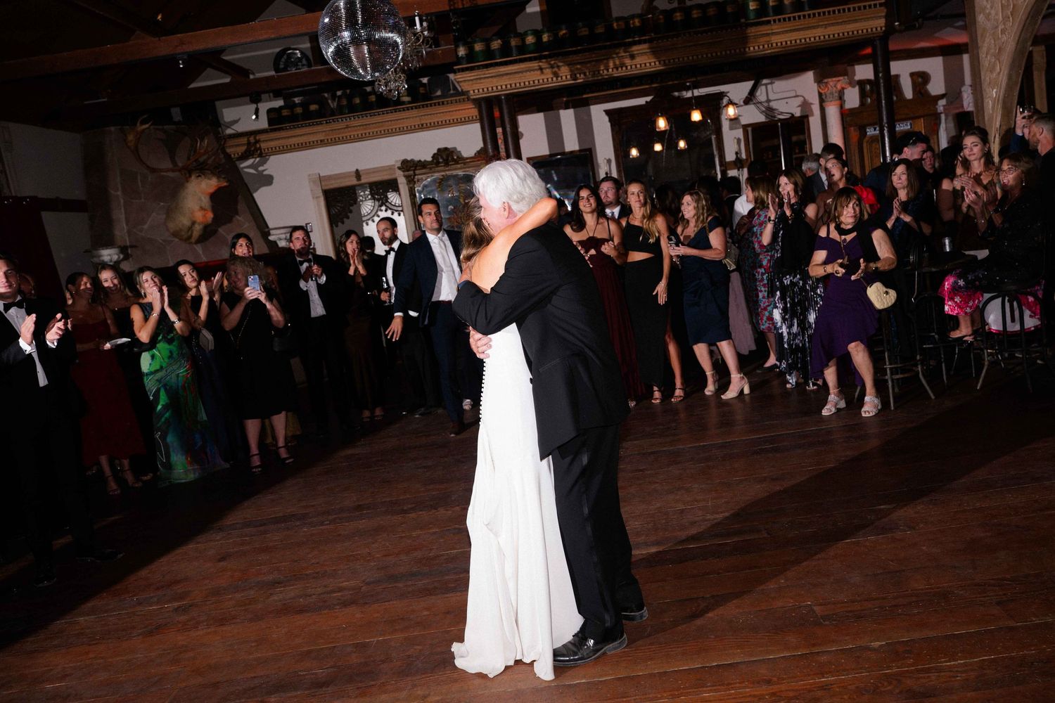 Elegant couple sharing a first dance at wedding reception surrounded by applauding guests.