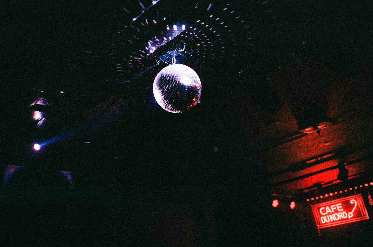 Glittering disco mirror ball hanging from ceiling inside dark nightclub with Cafe du Nord neon sign.