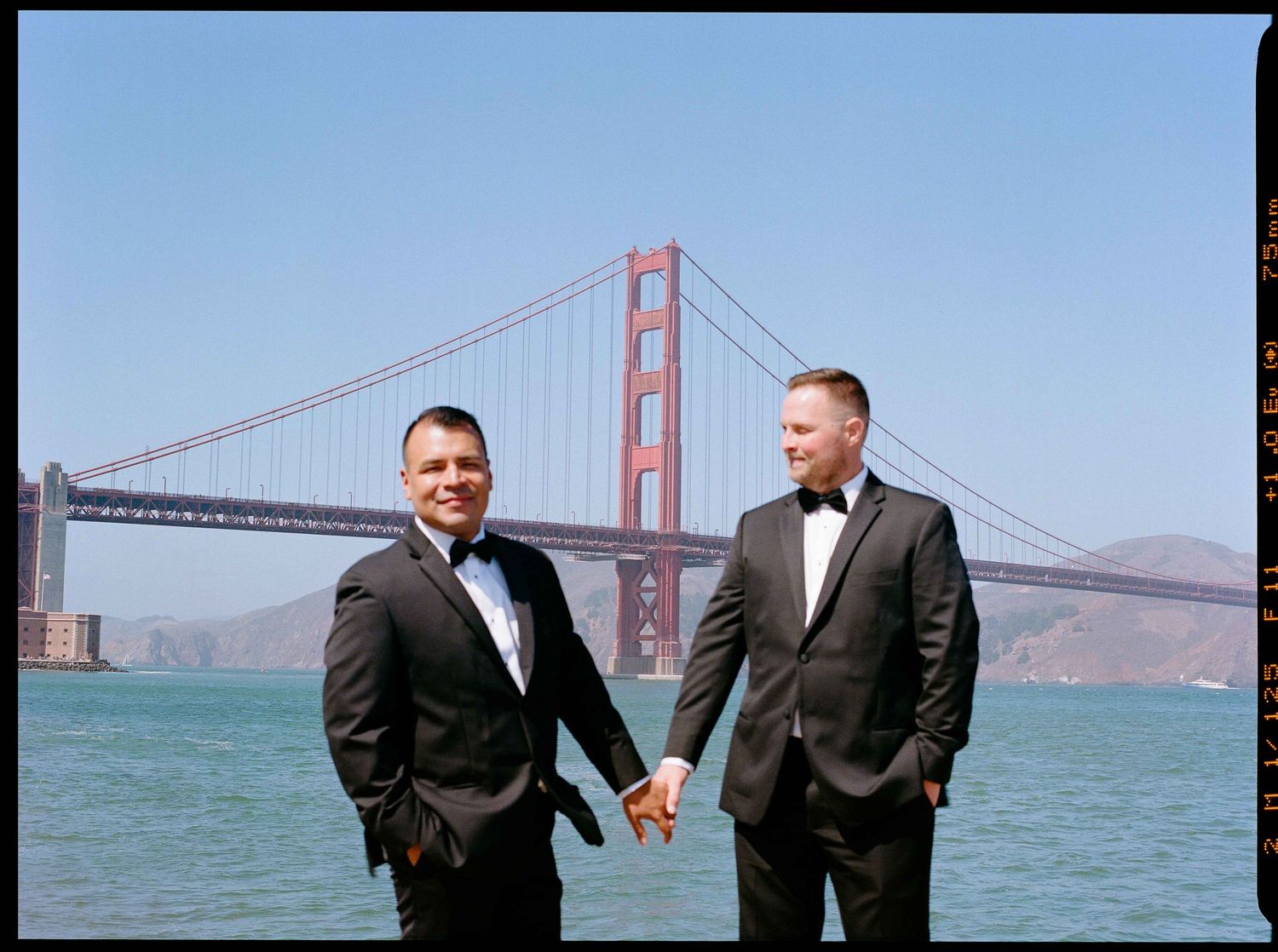 Grooms holding hands in front of the Golden Gate Bridge.