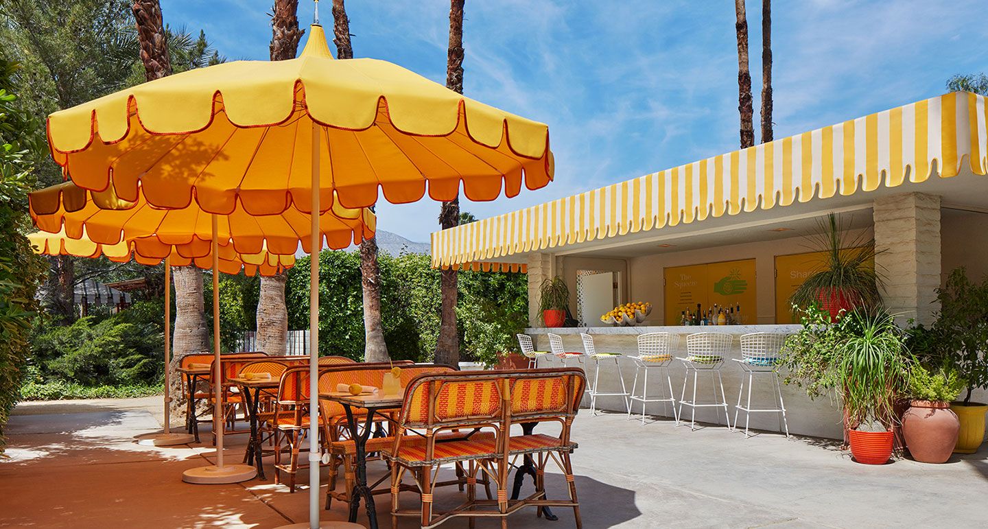 Vibrant yellow striped outdoor bar and patio area with colorful umbrellas and rattan chairs at a resort.