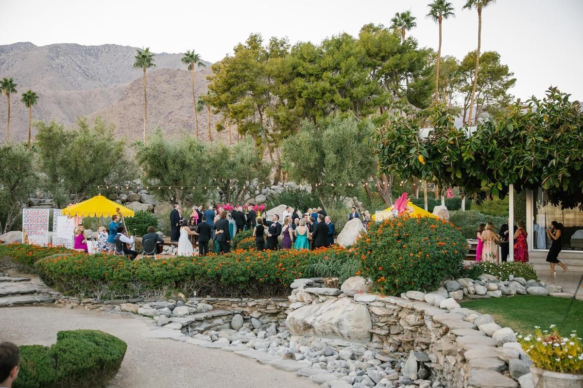 Outdoor garden wedding reception with guests gathered among lush landscaping and mountain views in Palm Springs.