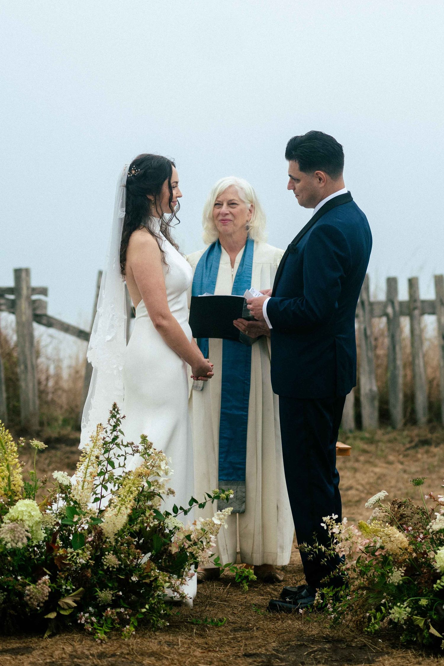 Wedding ceremony with an officiant and couple surrounded by floral arrangements at the Barn Meadow at the Sea Ranch Lodge.