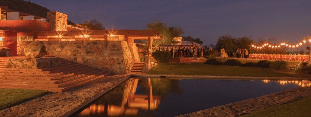 Frank Lloyd Wright's Taliesin West illuminated at night with string lights reflecting in a serene pool in the Arizona desert.