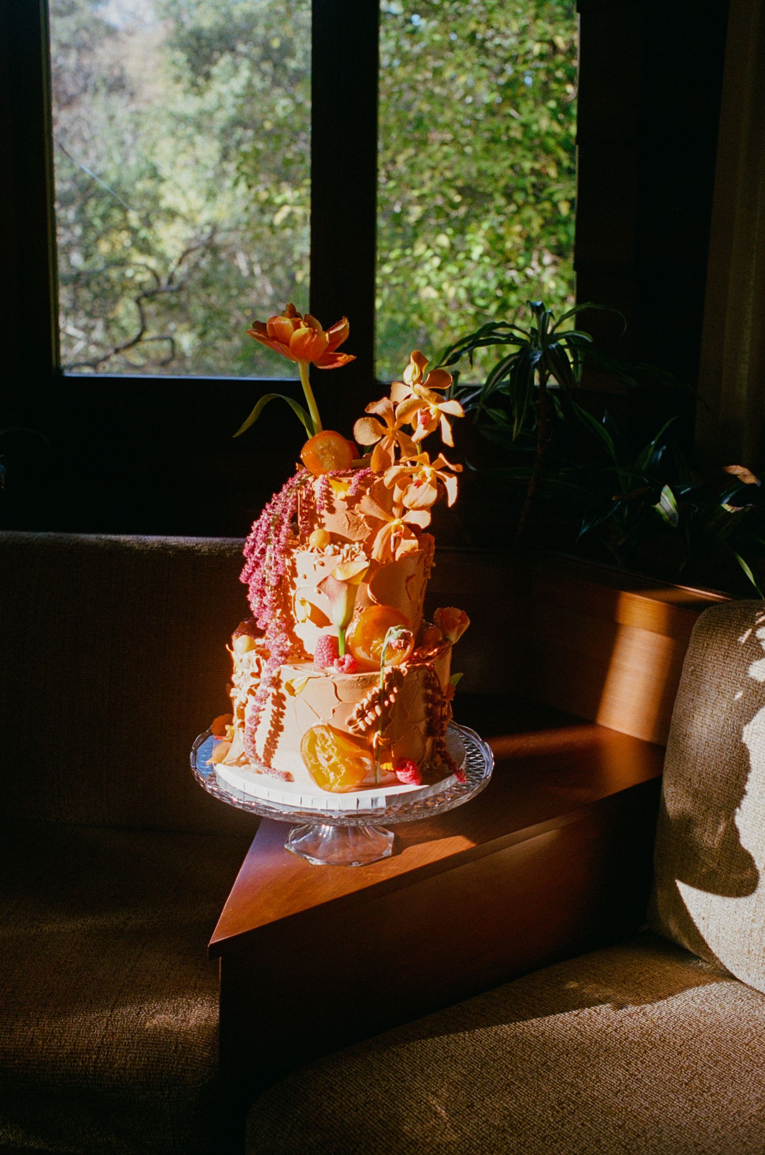 Funky orange three-tiered floral wedding cake in wooden living room.