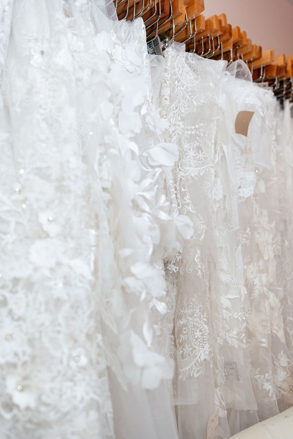 Wedding dresses with intricate lace details displayed on hangers in a bridal boutique.