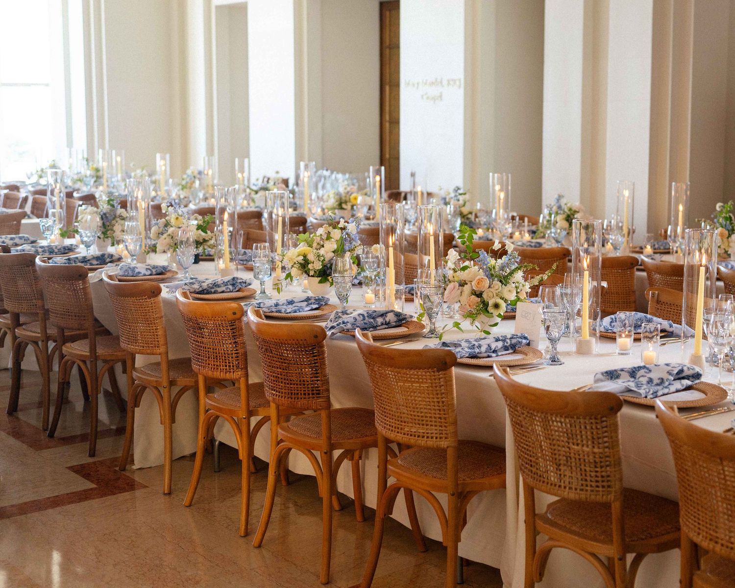 Long wedding reception table setup in mansion with tapered candles and blue napkins.