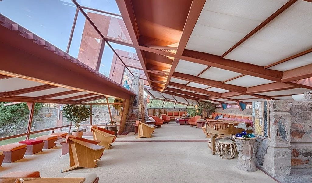 Frank Lloyd Wright-inspired interior with red wooden beams, geometric skylights, and mid-century modern furniture in an open pavilion.