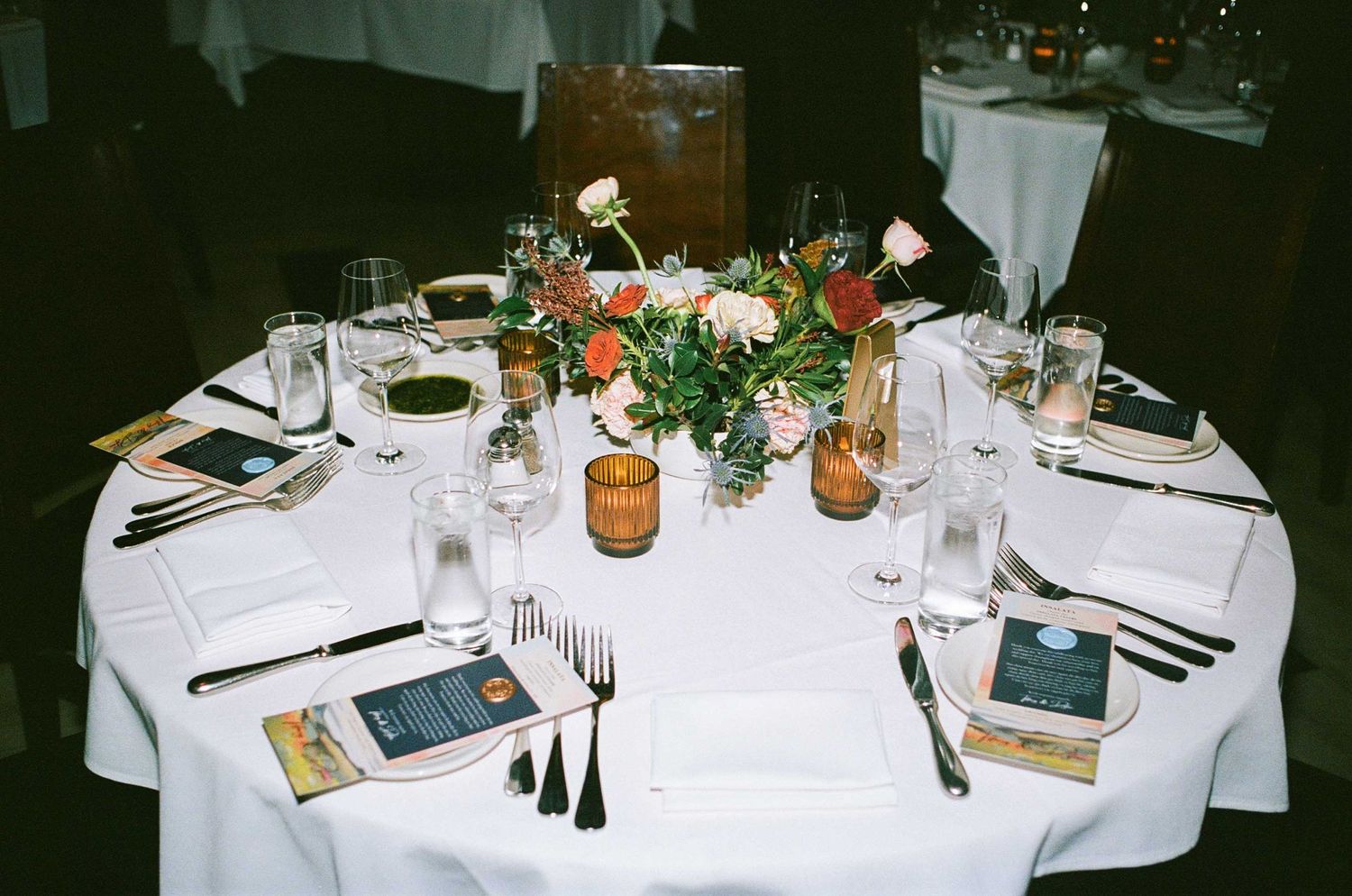 Round table with elegant place settings featuring floral centerpiece and glowing candles.