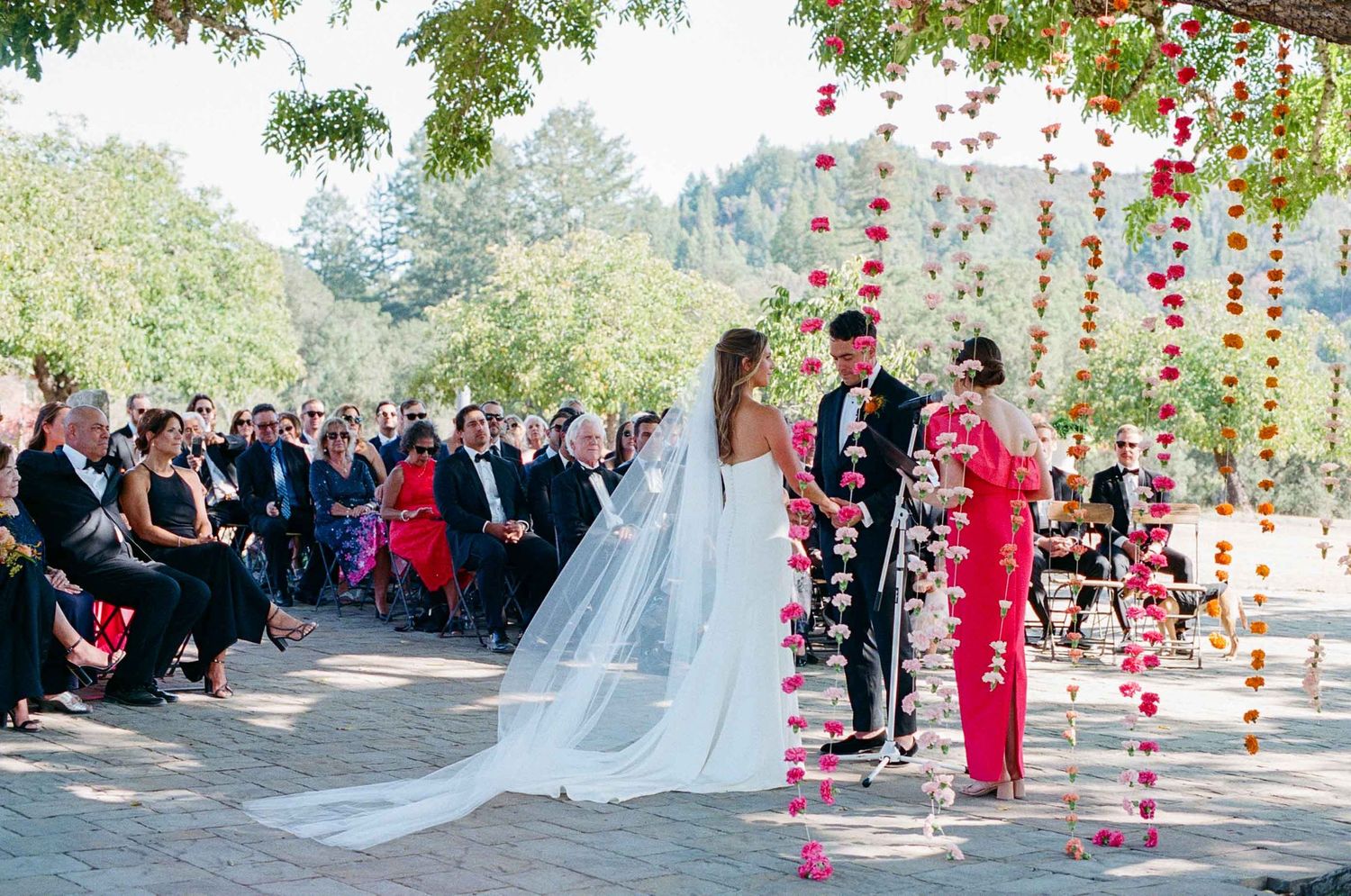 Bride and groom exchange vows under a floral arch with hanging blooms at an outdoor wedding.