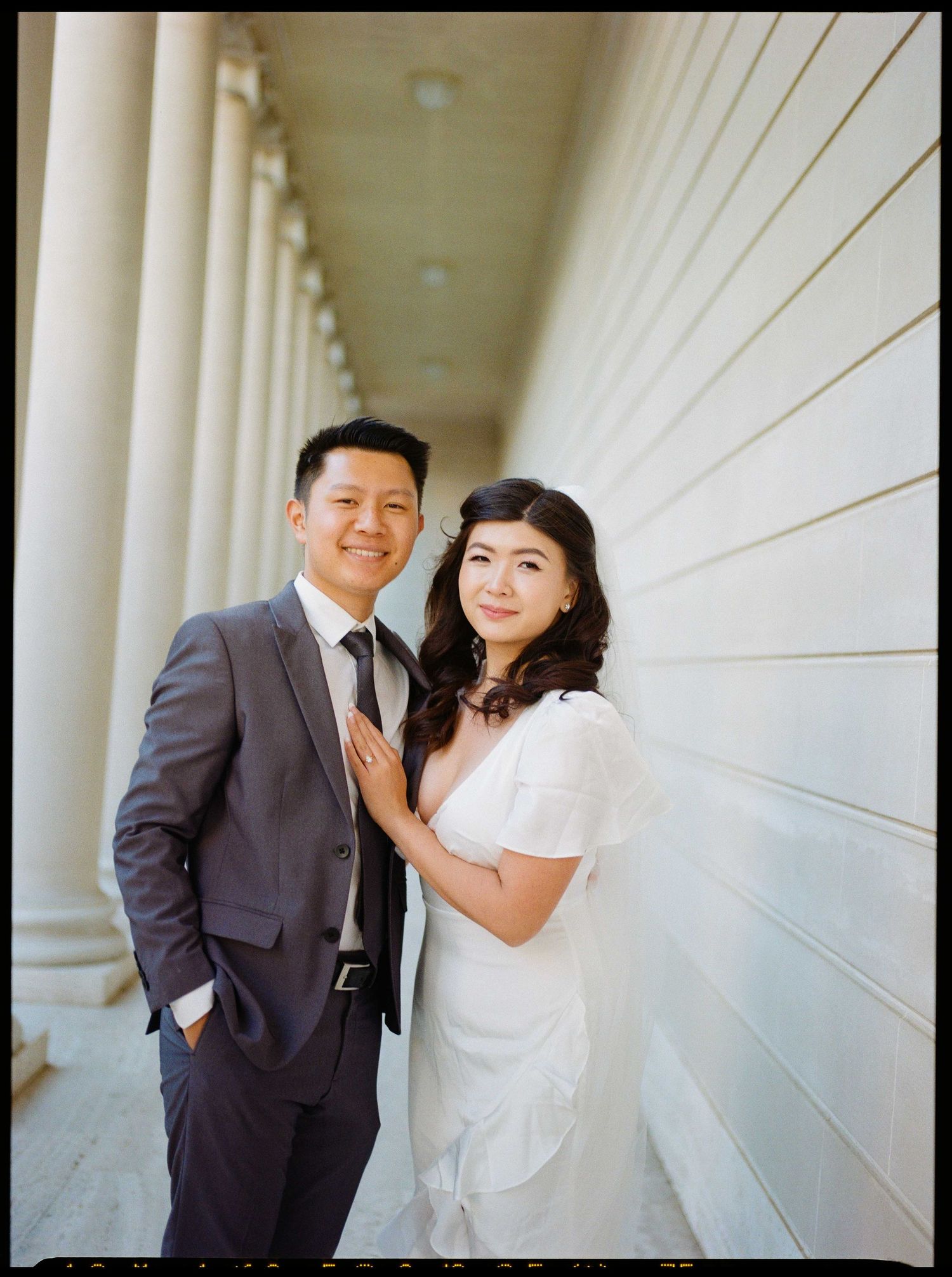 Wedding portrait at elegant colonnade with white pillars and walls creating striking geometry at the Legion of Honor.