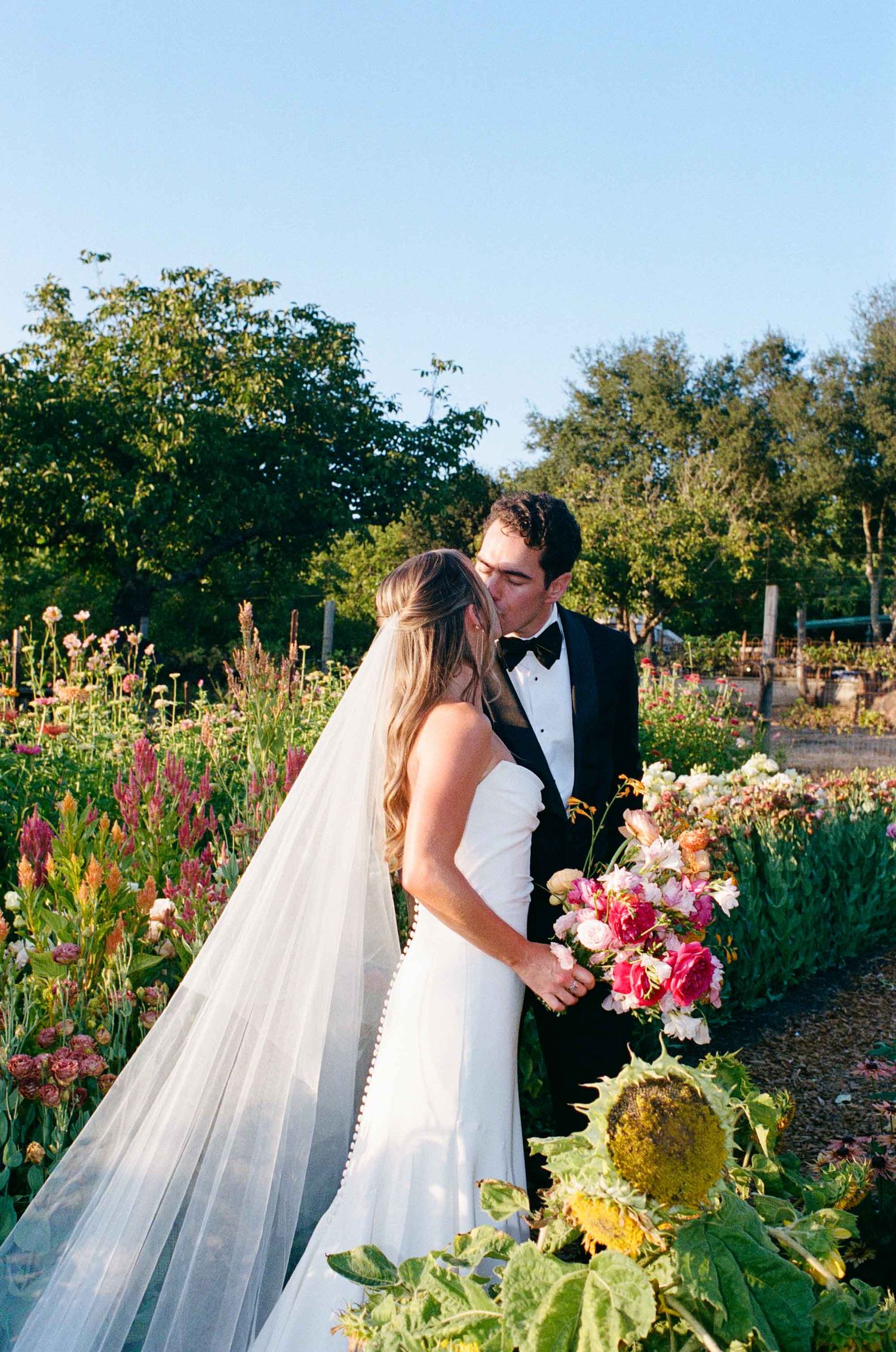 Bride and groom sharing a romantic moment in a vibrant flower garden, bride holding a colorful bouquet.
