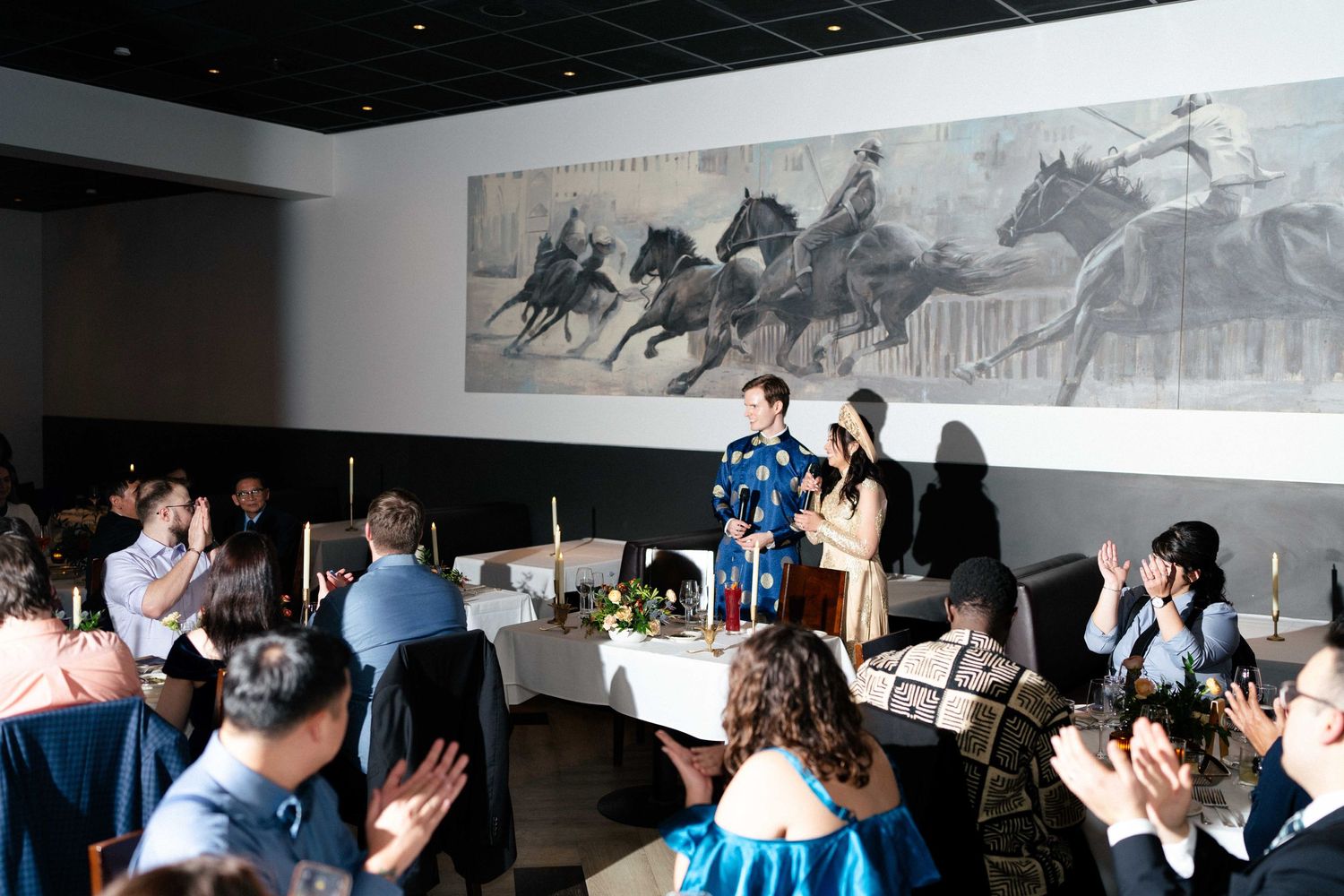 Guests gather at elegant tables in a dining room with a large horse-themed artwork displayed on the wall.