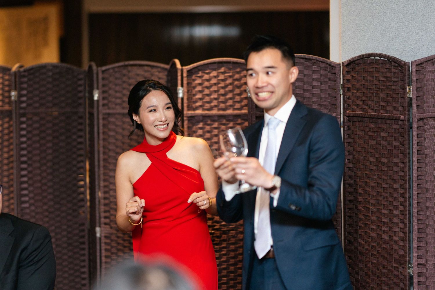 A couple toasts with wine glasses at an elegant event with decorative screens in the background.