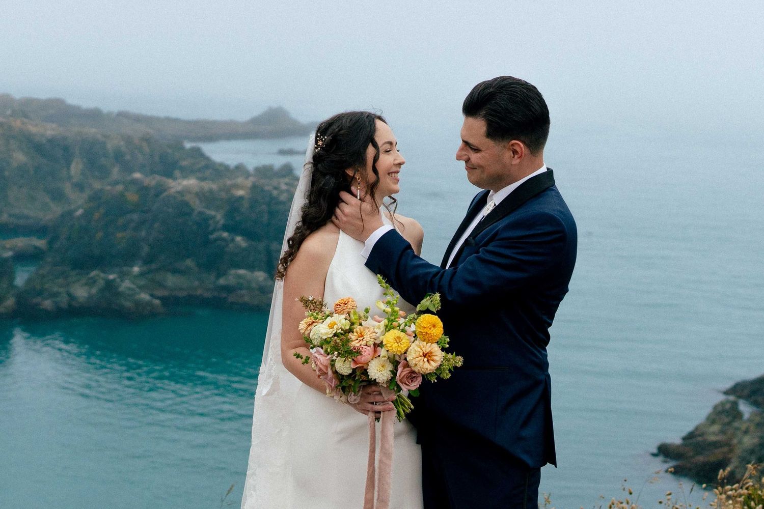 A couple embracing at their wedding in front of the Pacific Ocean.