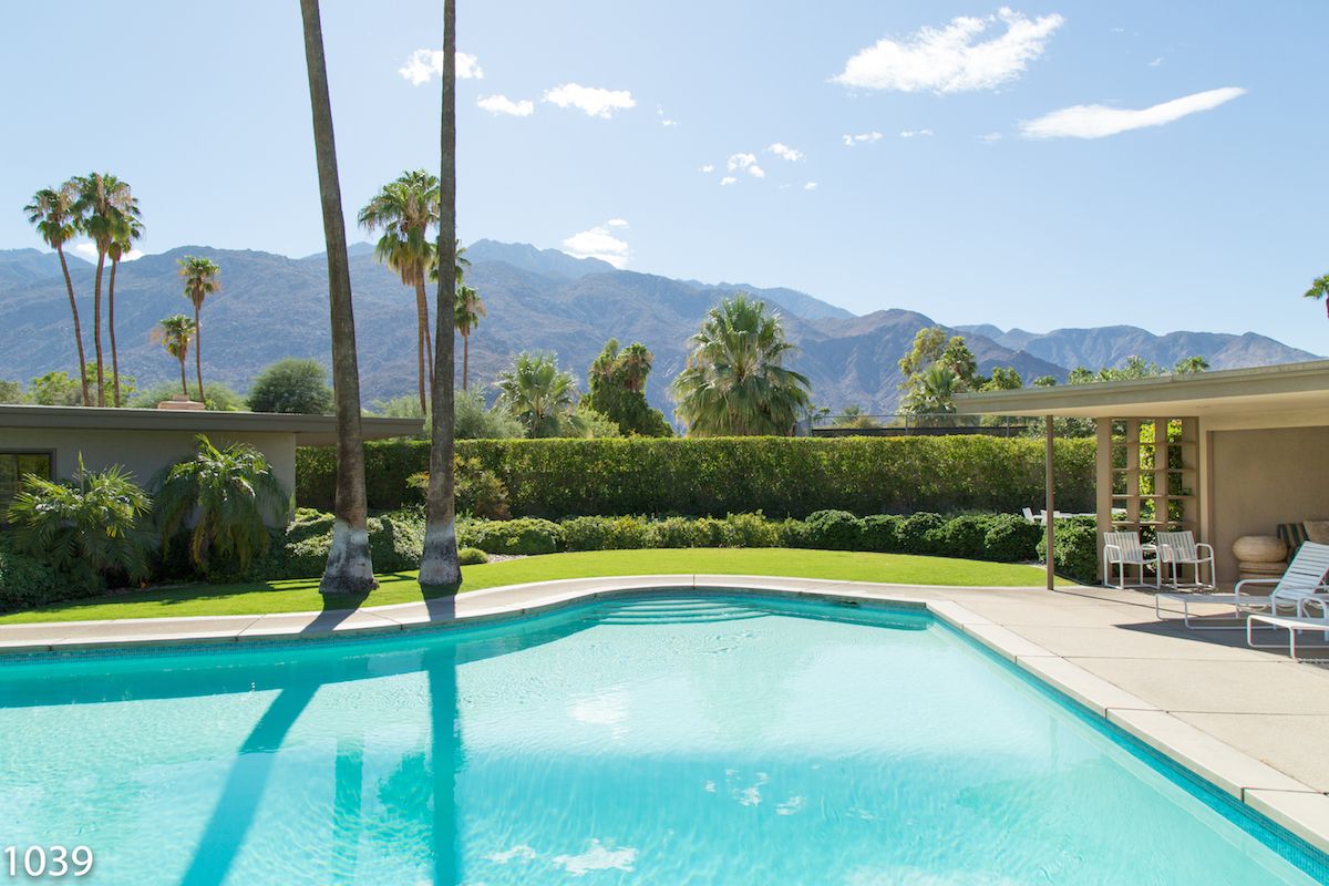 Turquoise swimming pool with mountain views, palm trees, and manicured hedges in Palm Springs, California.