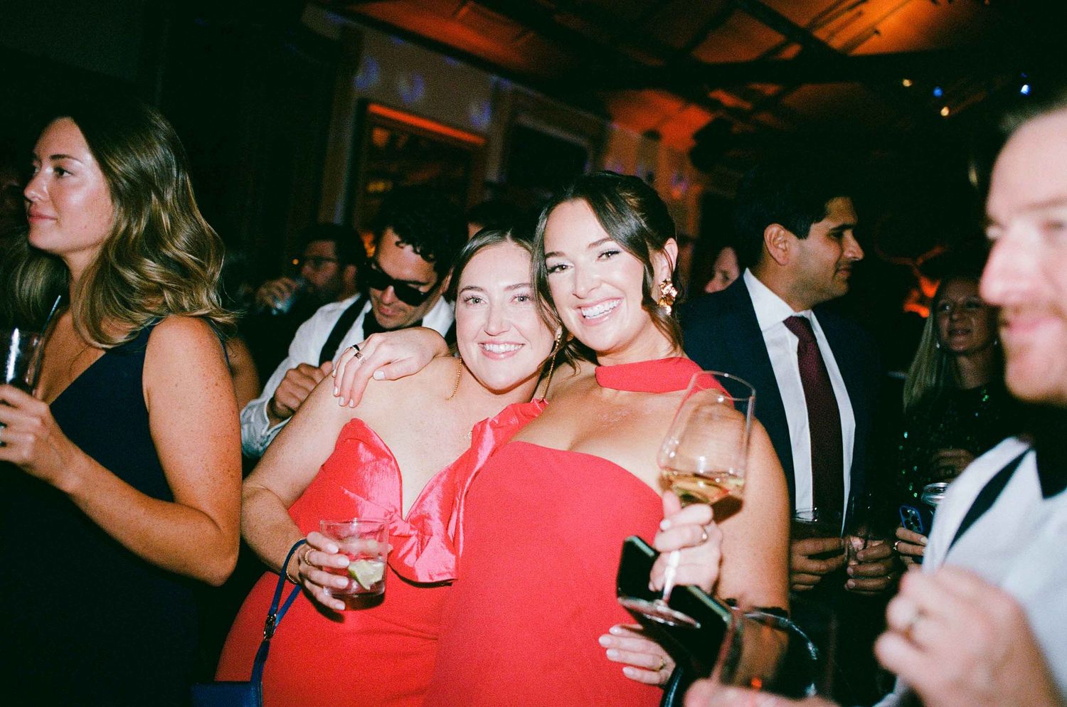 Two women in red dresses smiling and posing together at a wedding reception party.