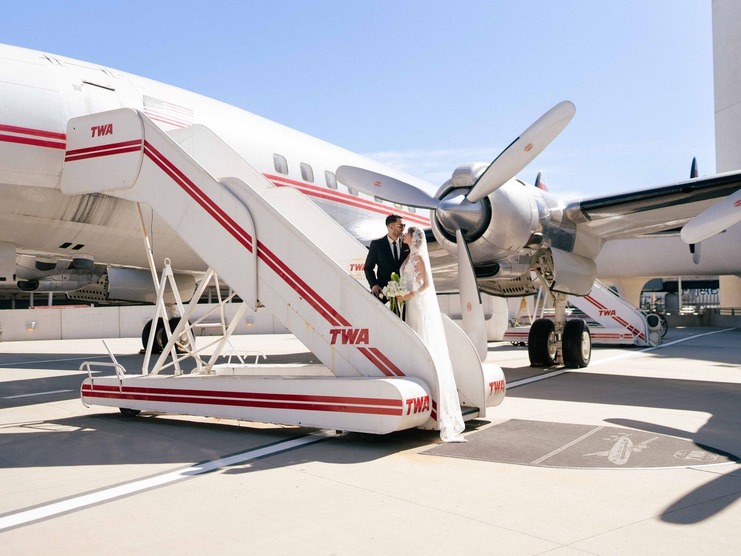 Newlyweds pose in front of a vintage TWA aircraft on their wedding day.