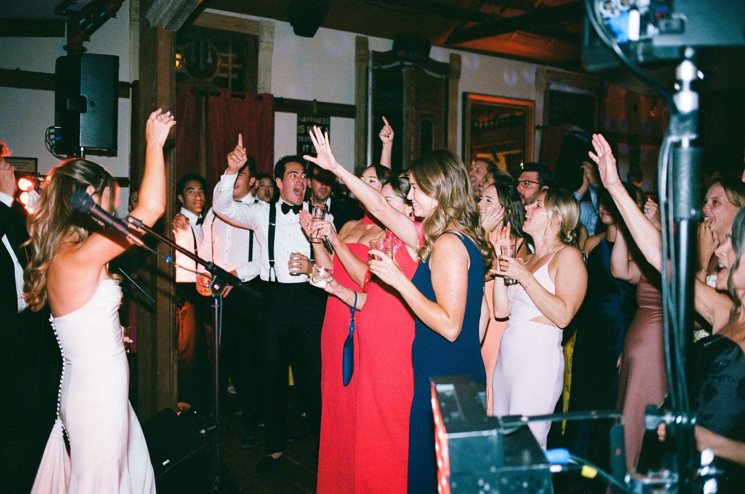 Energetic wedding reception dance floor with guests and band performing under warm lights.