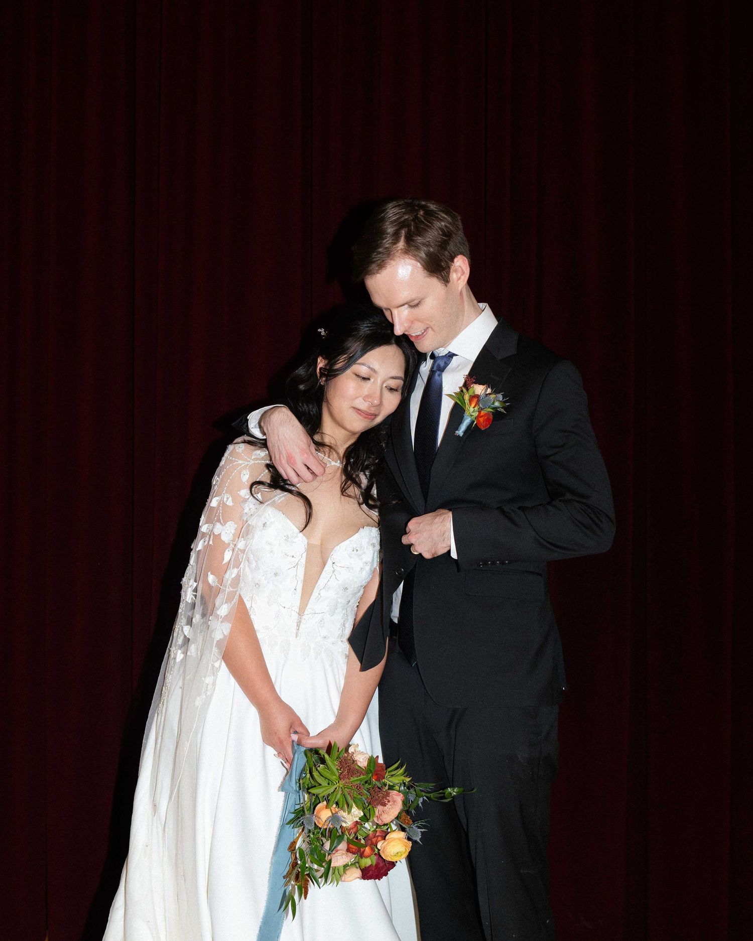 Intimate moment captured against a deep red curtain backdrop at a wedding reception.