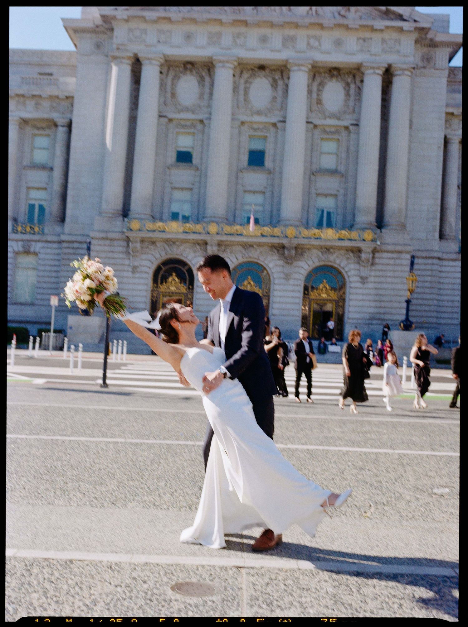 Dynamic wedding pose in front of San Francisco City Hall holding floral bouquet.
