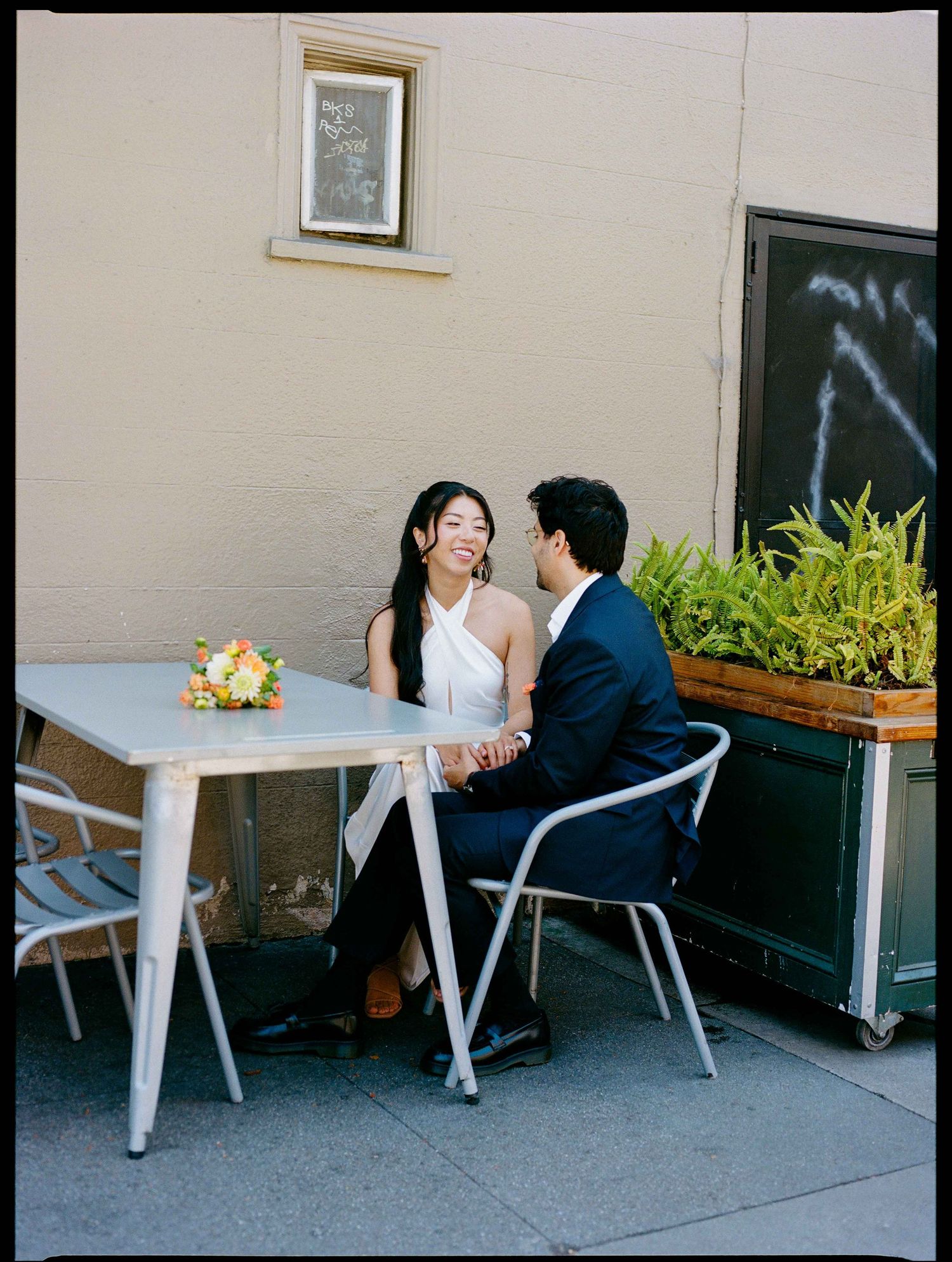 Couple holds hands at outdoor cafe table during romantic engagement photo session.