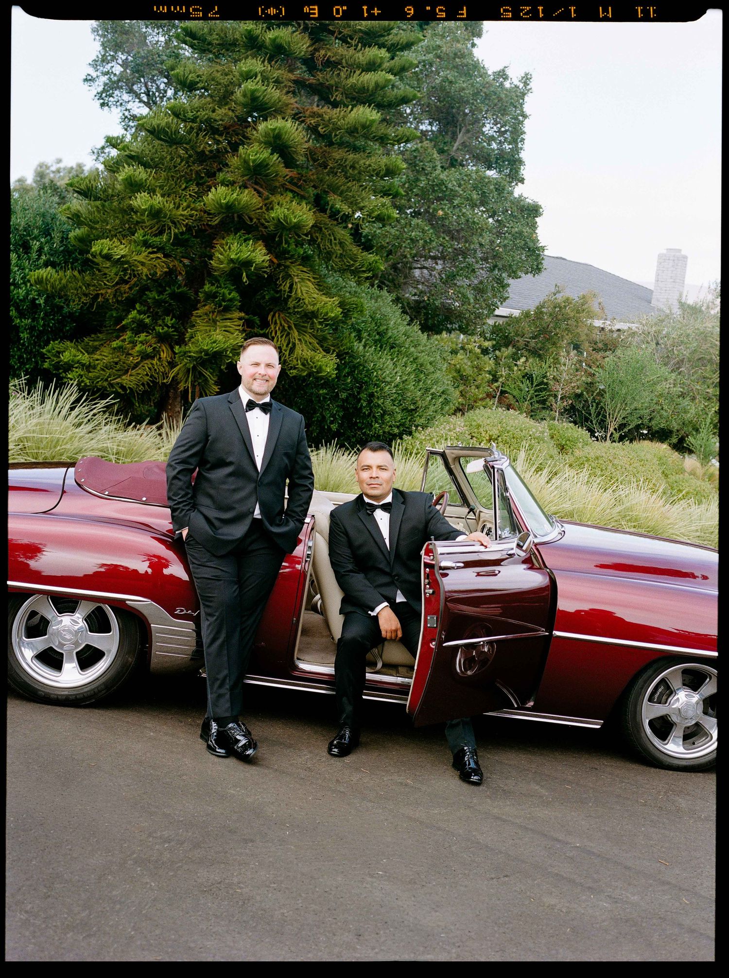 Grooms next to each other in vintage red car.