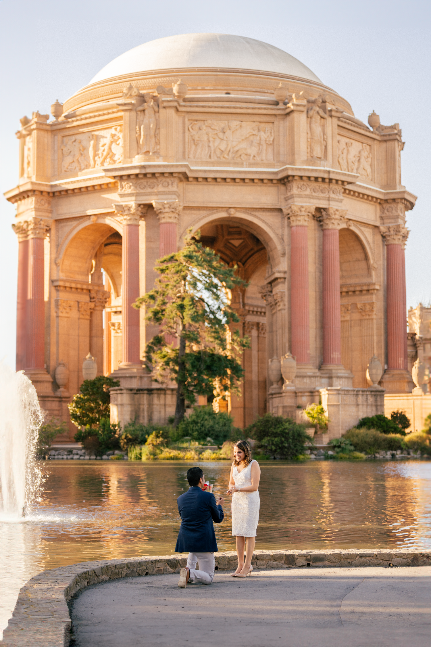 A proposal moment at the Palace of Fine Arts in San Francisco with its iconic dome and reflection pool at sunset.