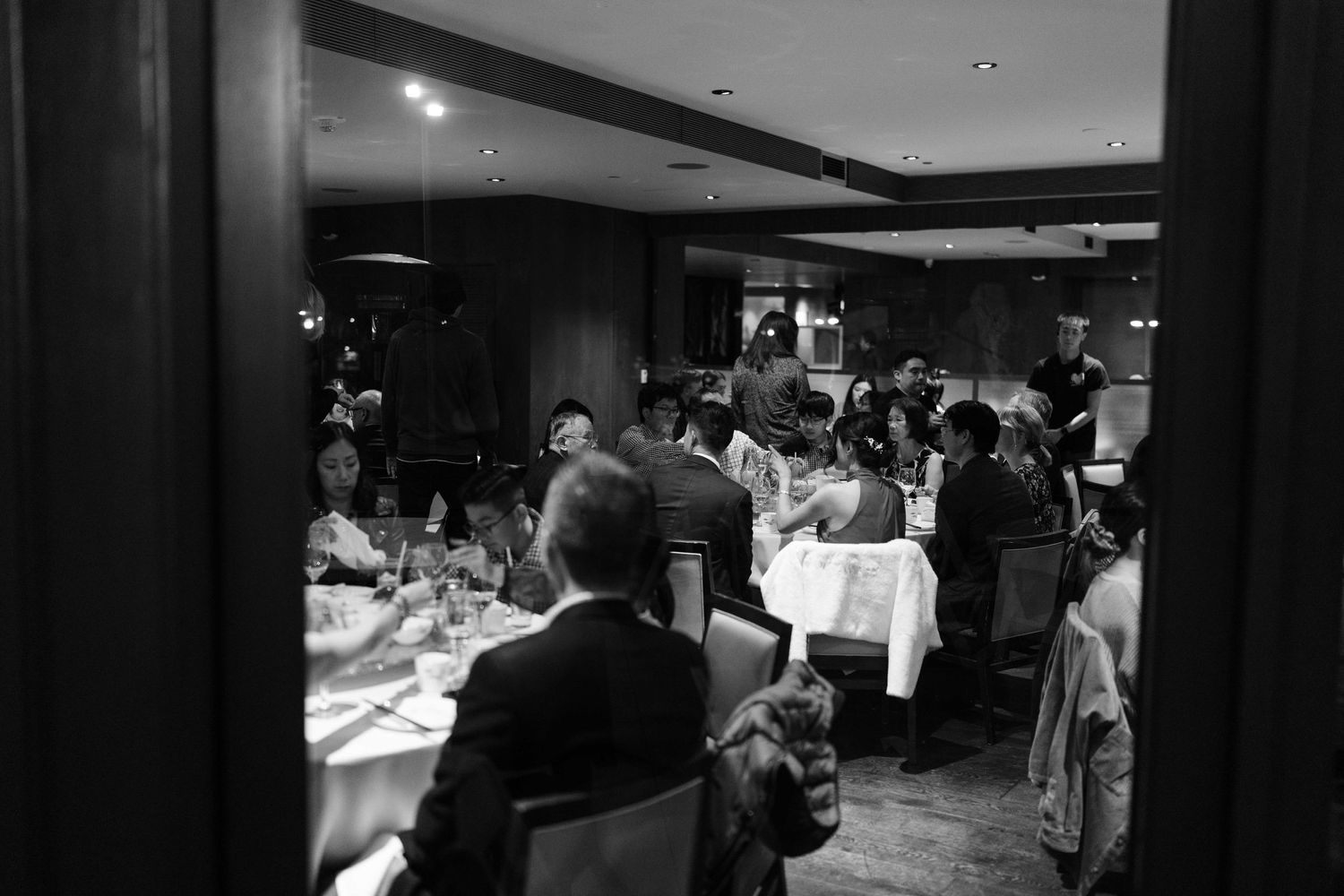 Black and white photo of guests dining at an indoor wedding reception.