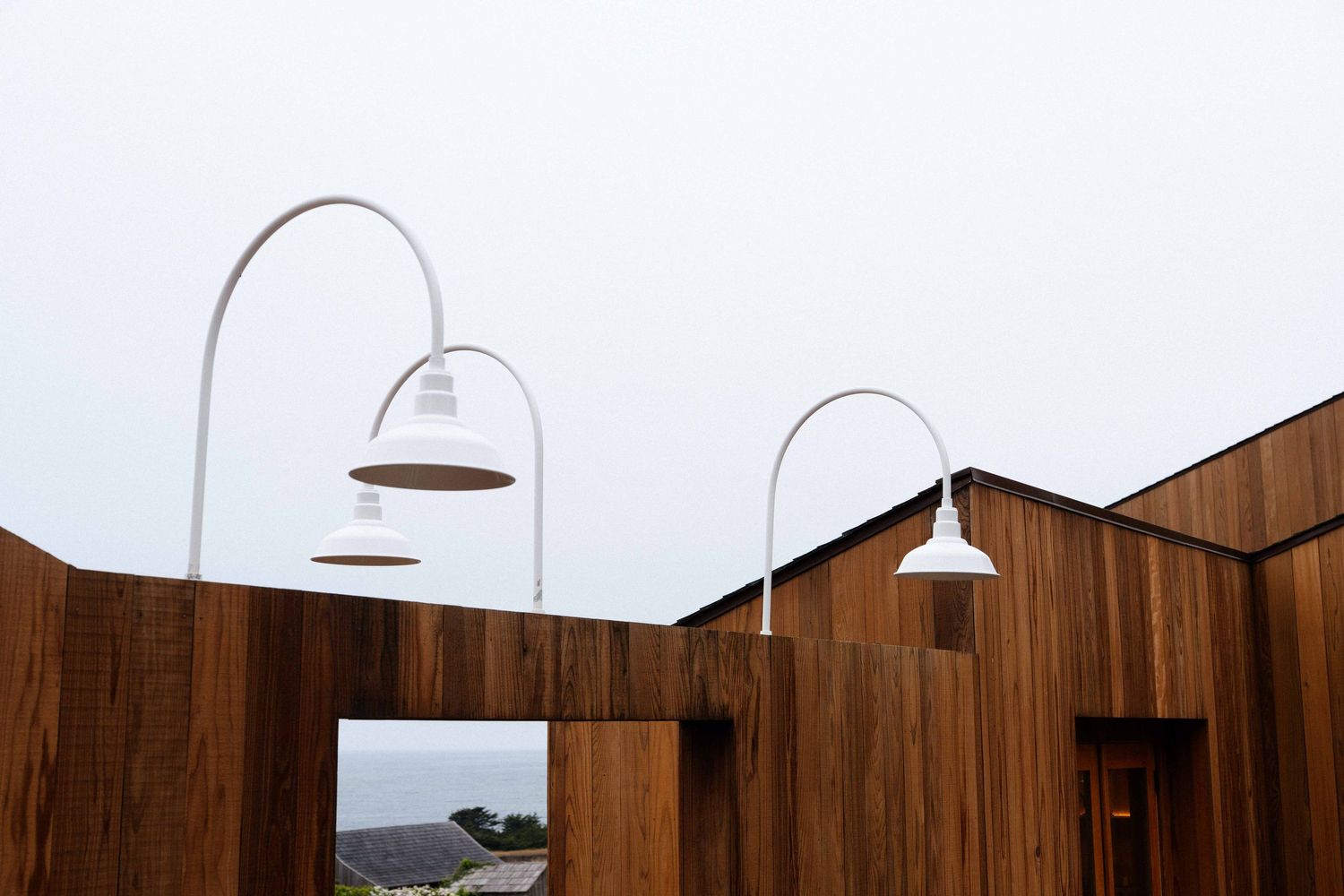 Modern wooden building exterior with white arched lamp posts against an overcast sky.