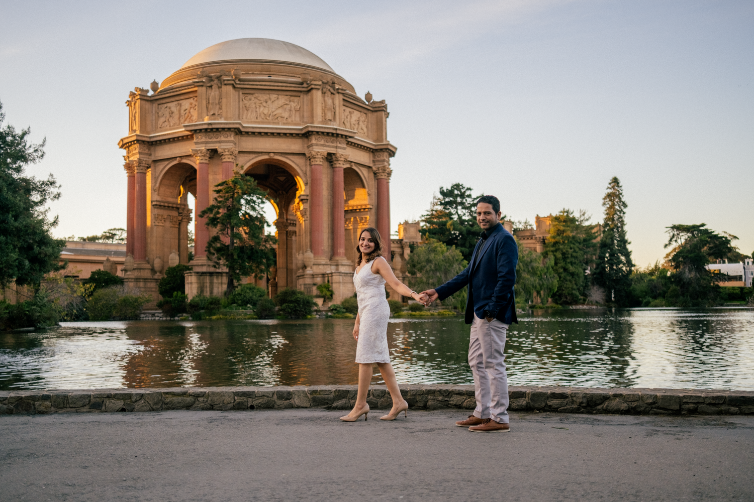 A romantic couple stands together at the Palace of Fine Arts in San Francisco during golden hour.