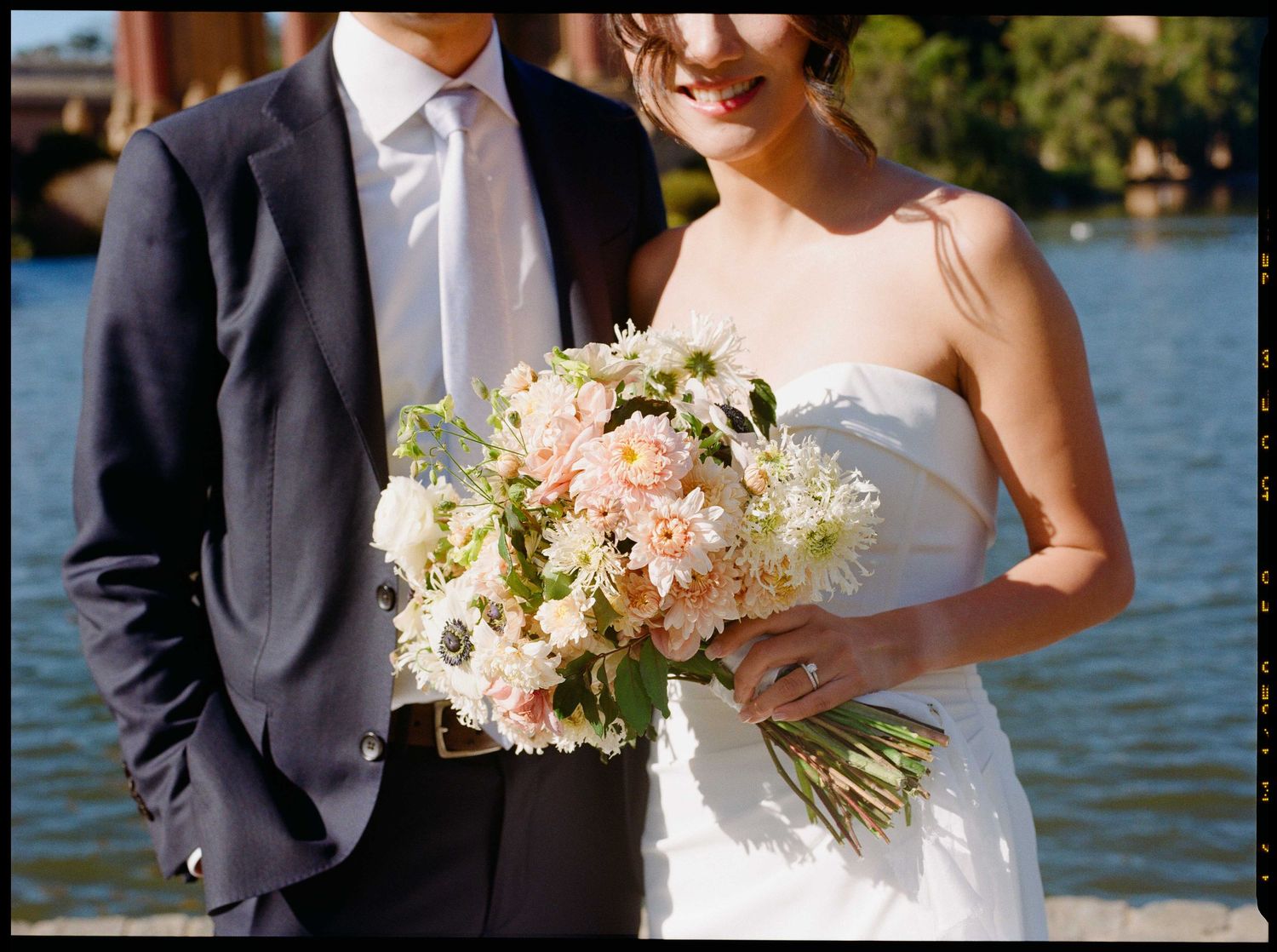 Wedding couple holding a delicate pink and white bouquet against a the lake at the Palace of Fine Arts