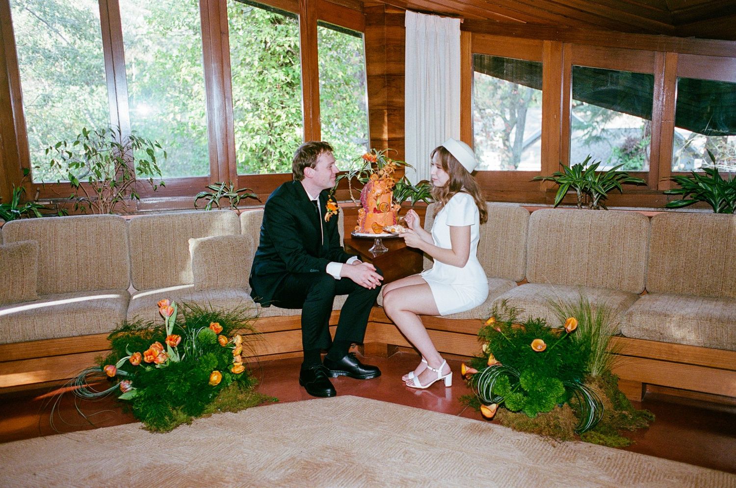 Couple cutting orange wedding cake in mid-century modern living room.