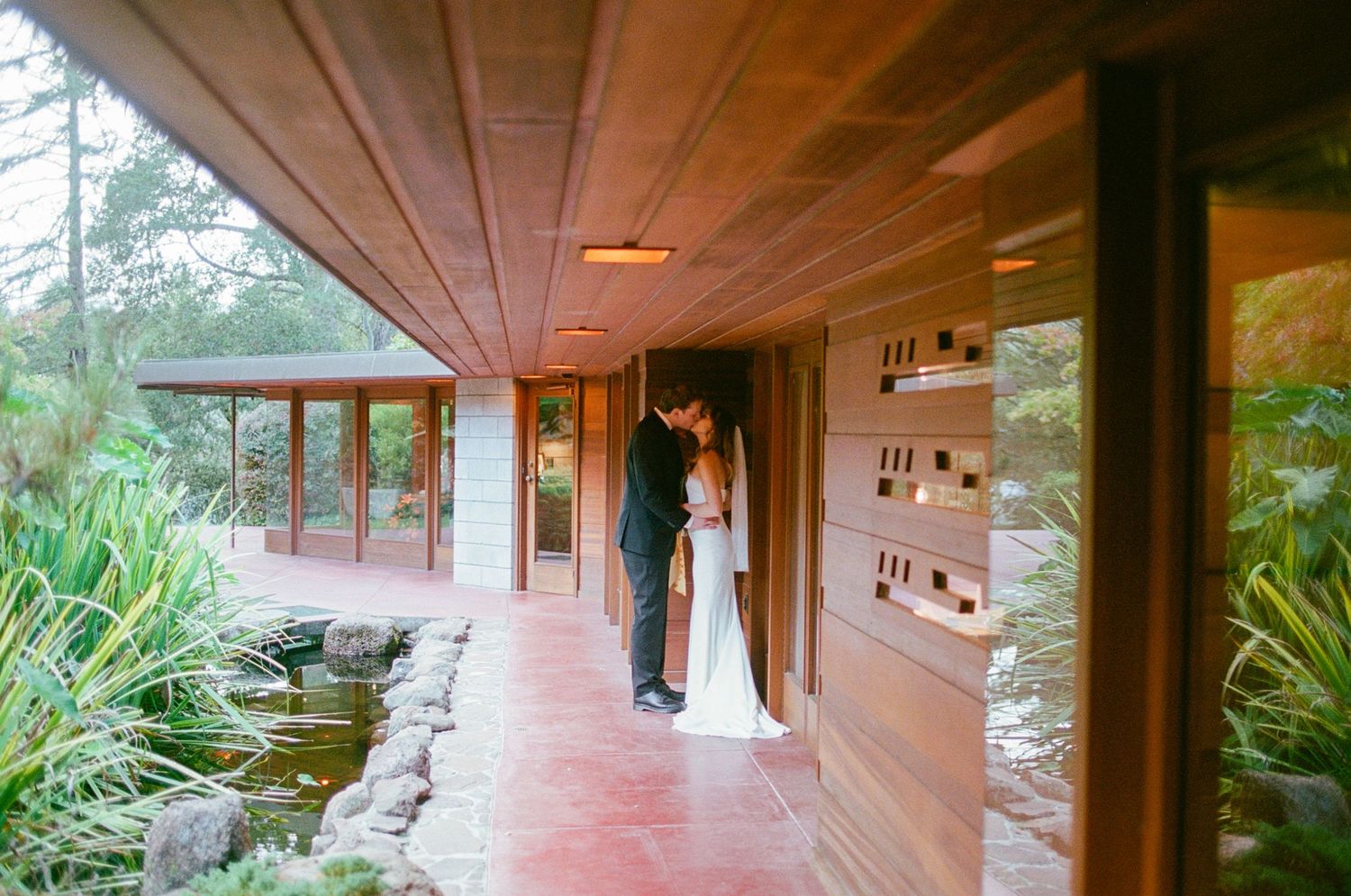 Bride and groom kissing against Frank Lloyd Wright house exterior hallway.
