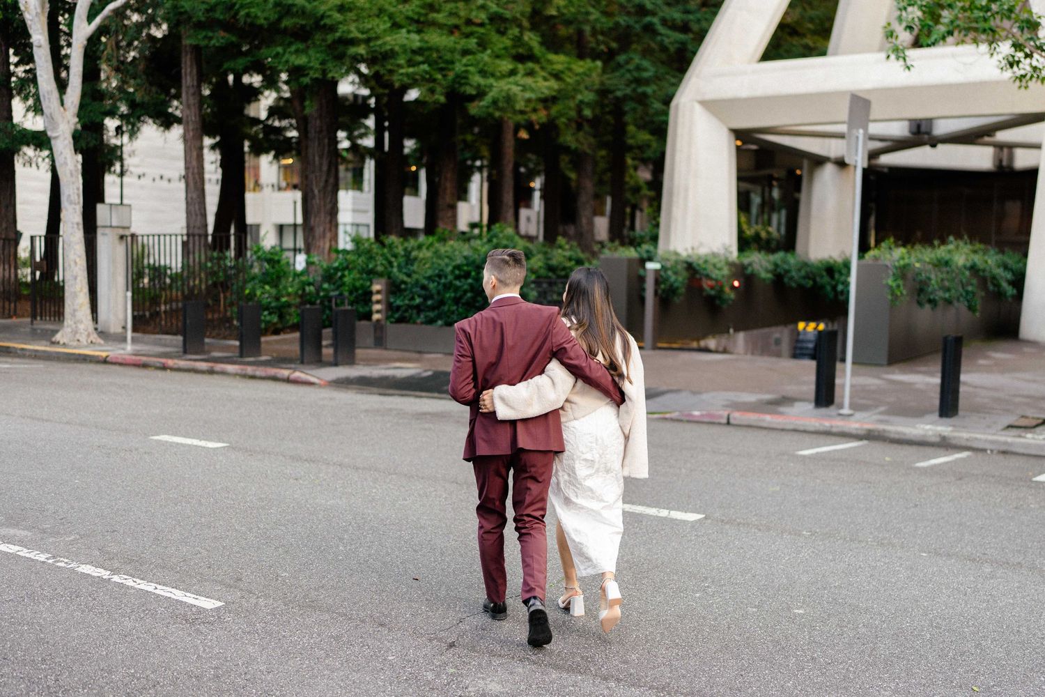 Couple strolling together on an urban street with trees in background.