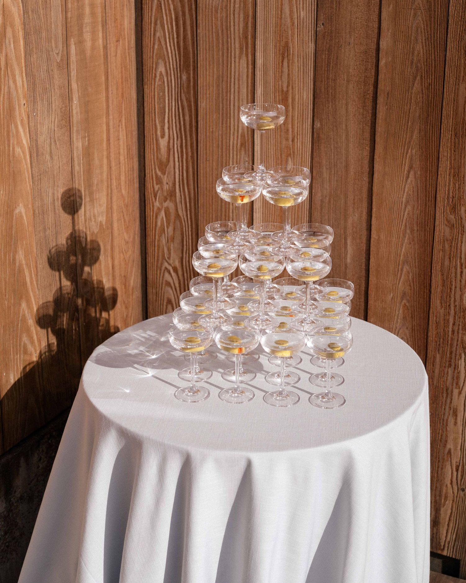 Elegant champagne tower with coupe glasses on a white draped table against a wooden wall backdrop.