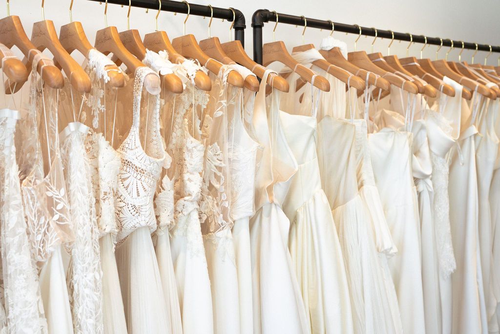 Row of elegant white wedding dresses hanging on wooden hangers in a bridal boutique.