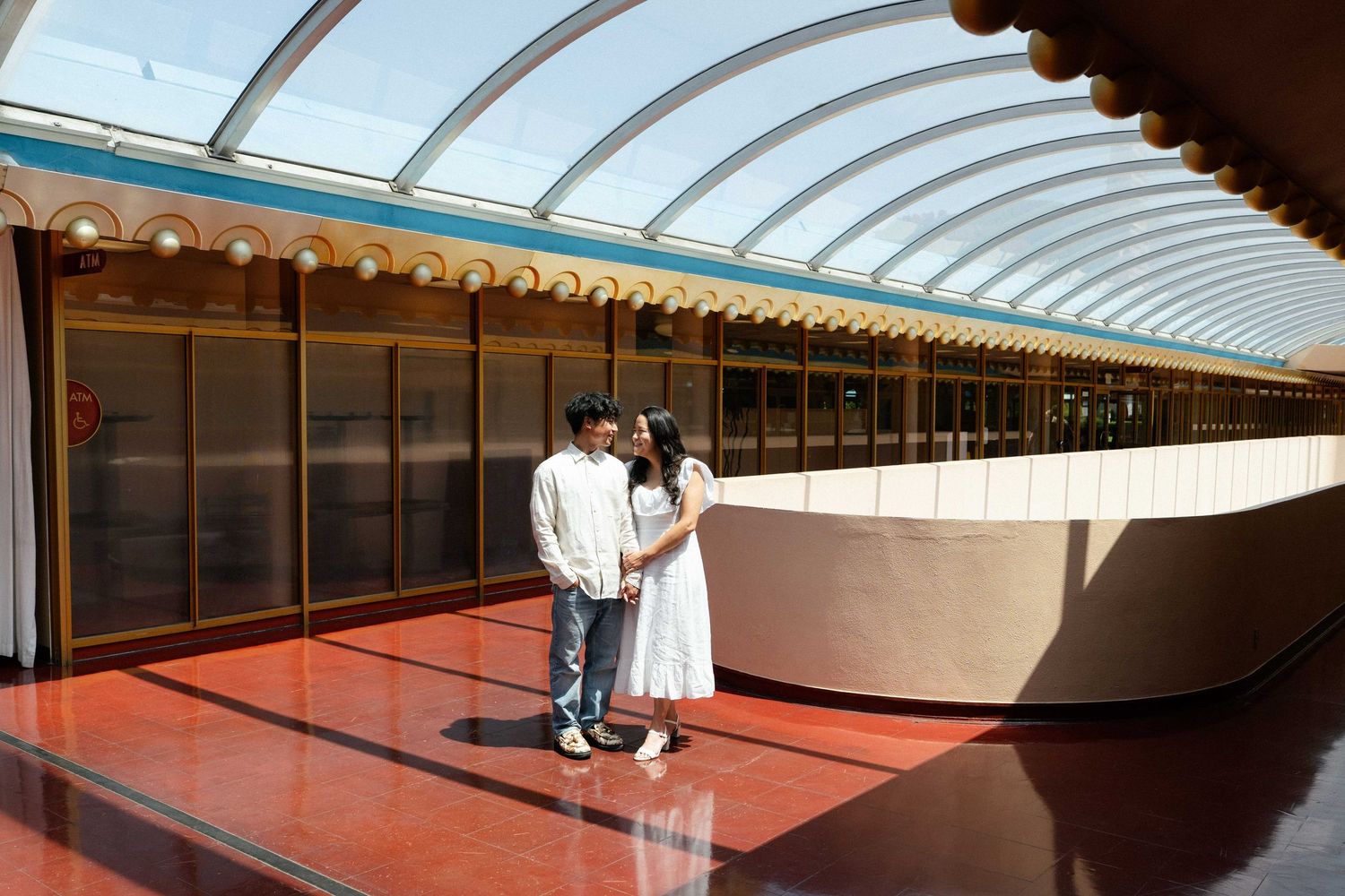 Couple posing together inside a modern architectural space with curved glass ceiling and red floor.