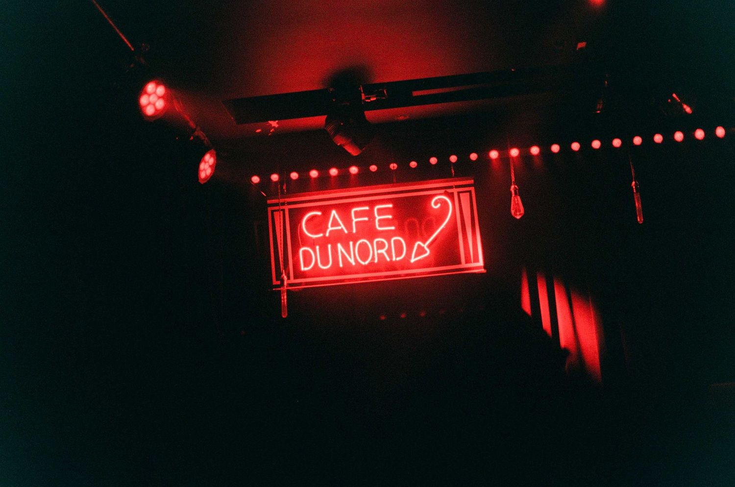 Red neon sign for Cafe Du Nord glowing in a dark venue with red accent lights along the ceiling.