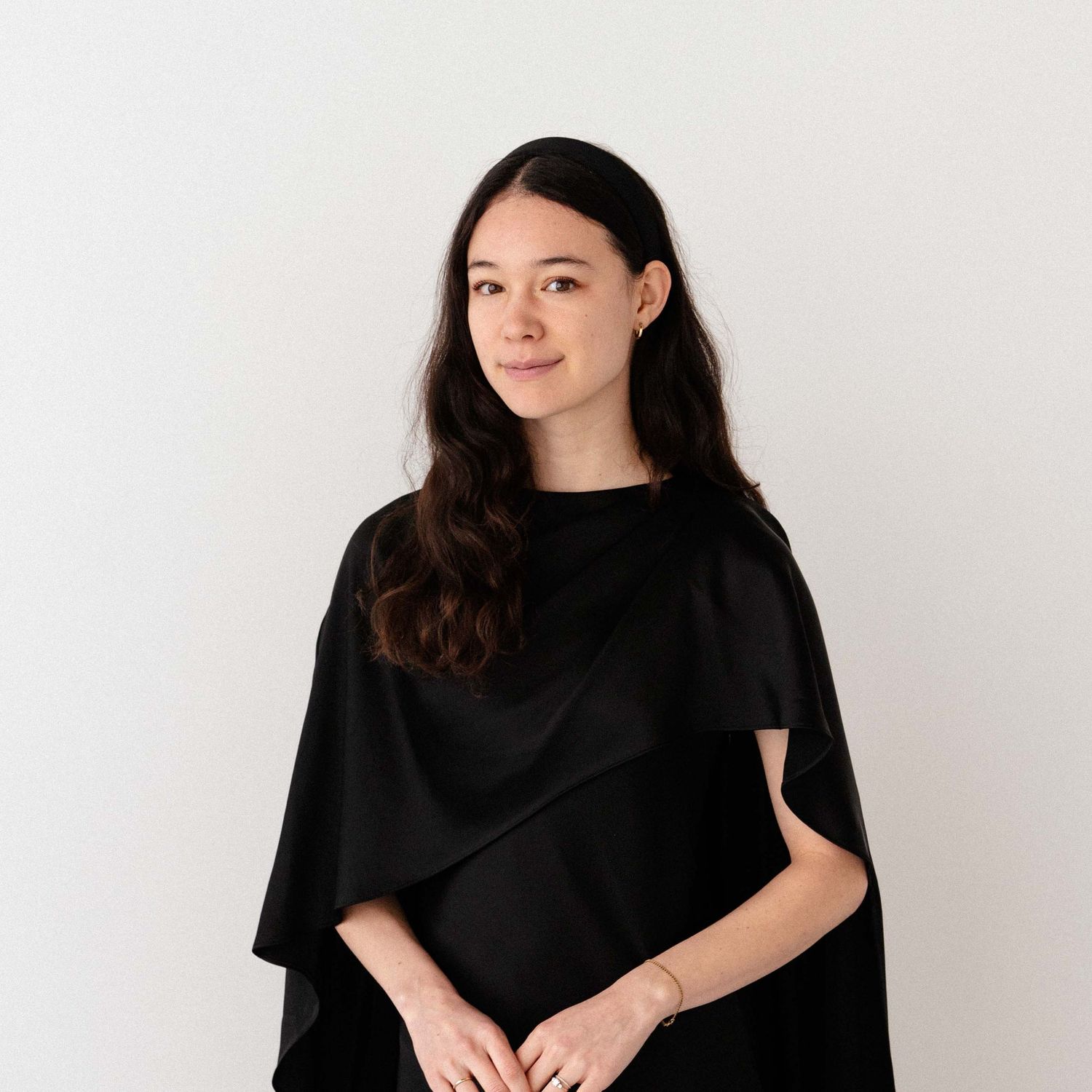 Professional portrait of a young woman in a black cape top against a clean white background.