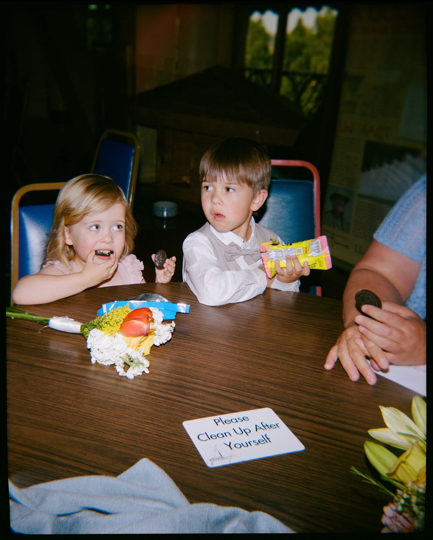 Two young children sitting at a table with flowers and snacks at a wedding reception.