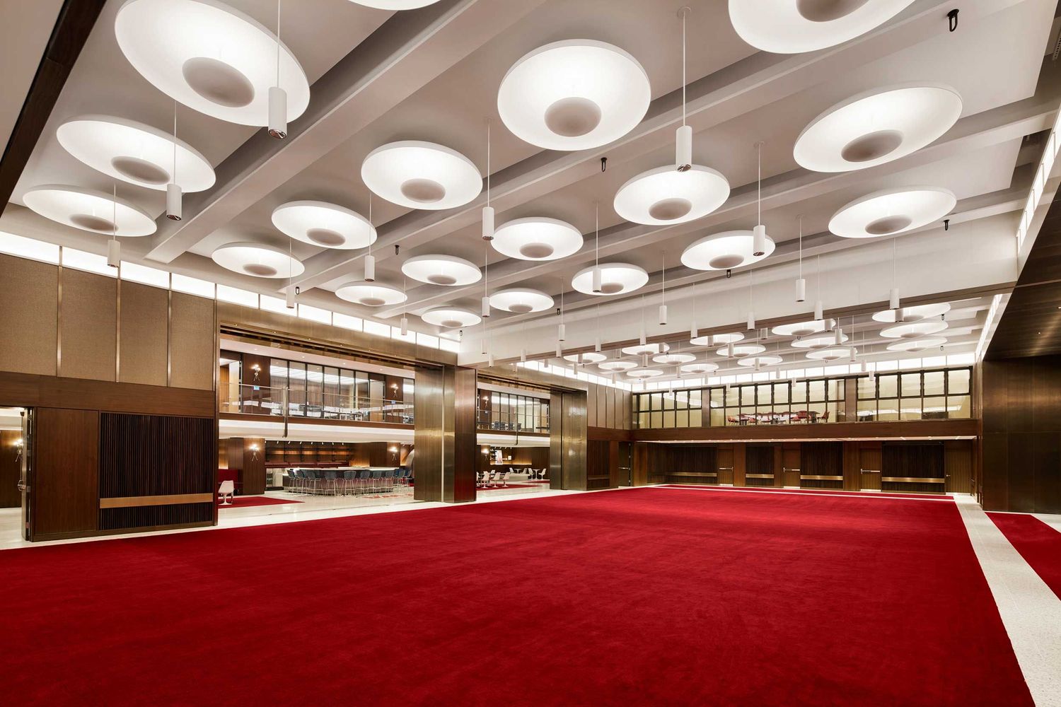 Elegant ballroom with circular pendant lights on white ceiling and vibrant red carpet flooring.