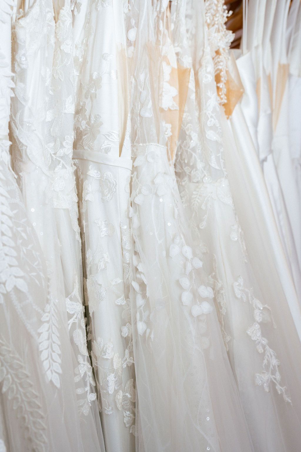 Close-up detail of delicate lace patterns on white wedding dresses hanging on display at Lace & Liberty in San Francisco.