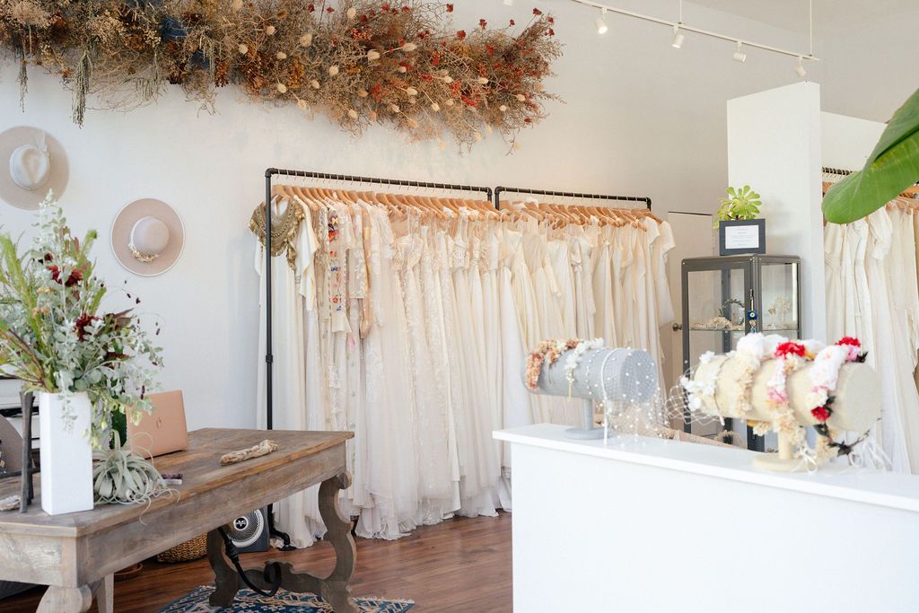 Bridal boutique interior with white dresses, dried floral decorations, and rustic furniture.