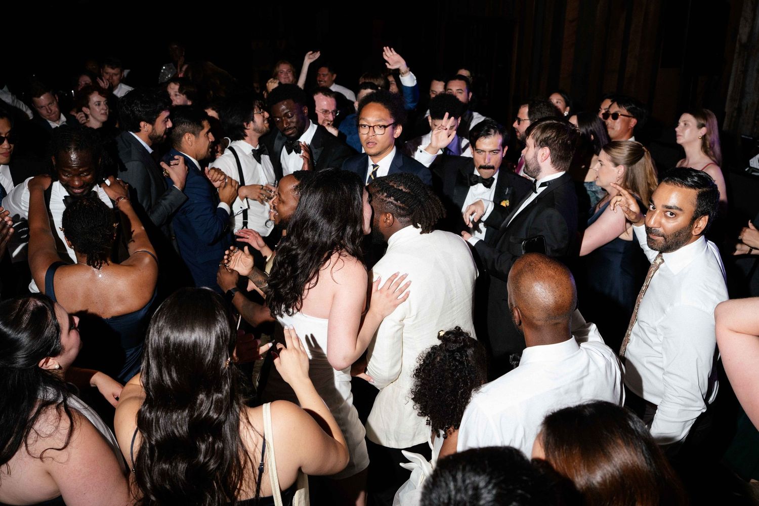 Diverse crowd of elegantly dressed guests dancing and celebrating at a formal wedding reception party.
