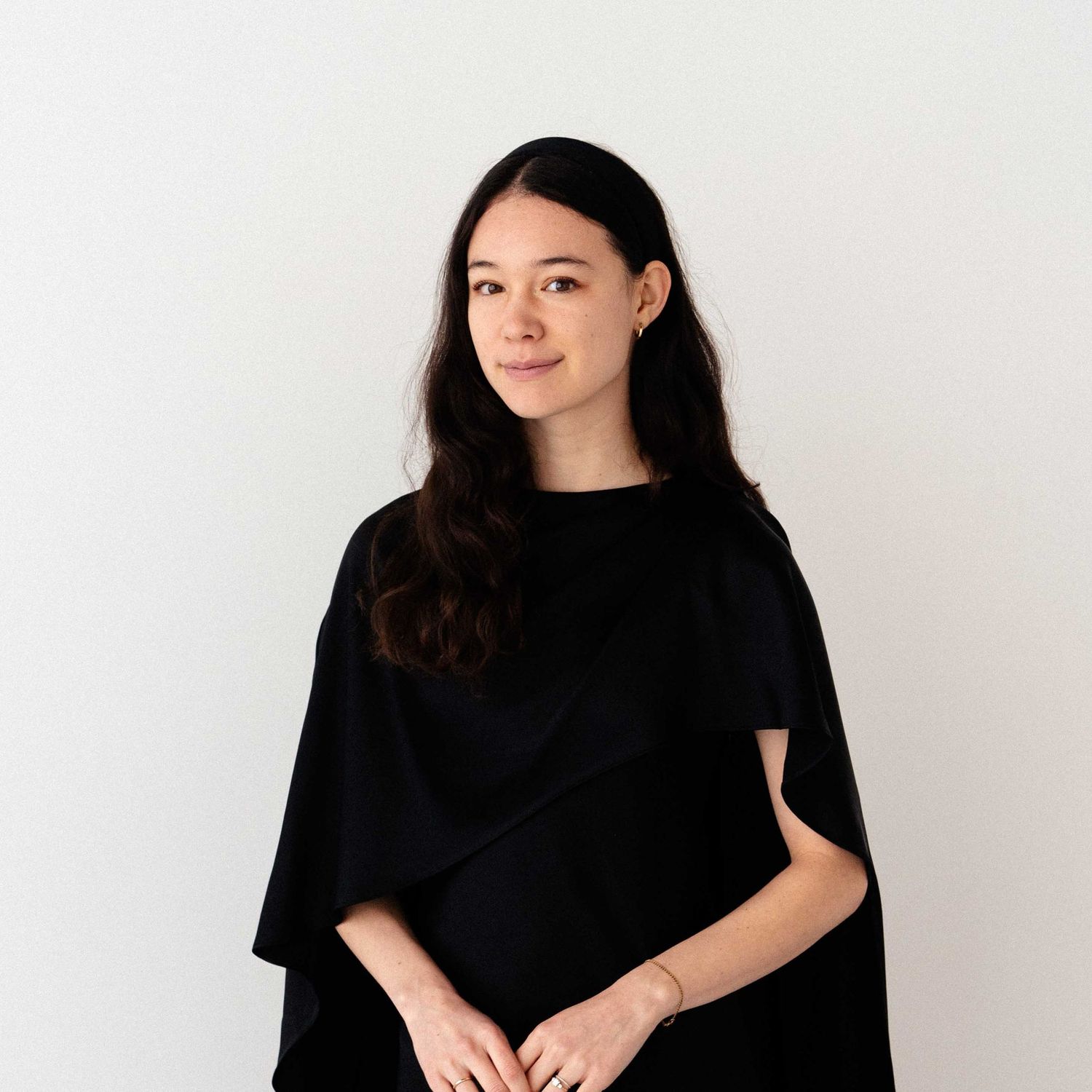Portrait of a woman with long dark hair wearing a black oversized top against a white background.