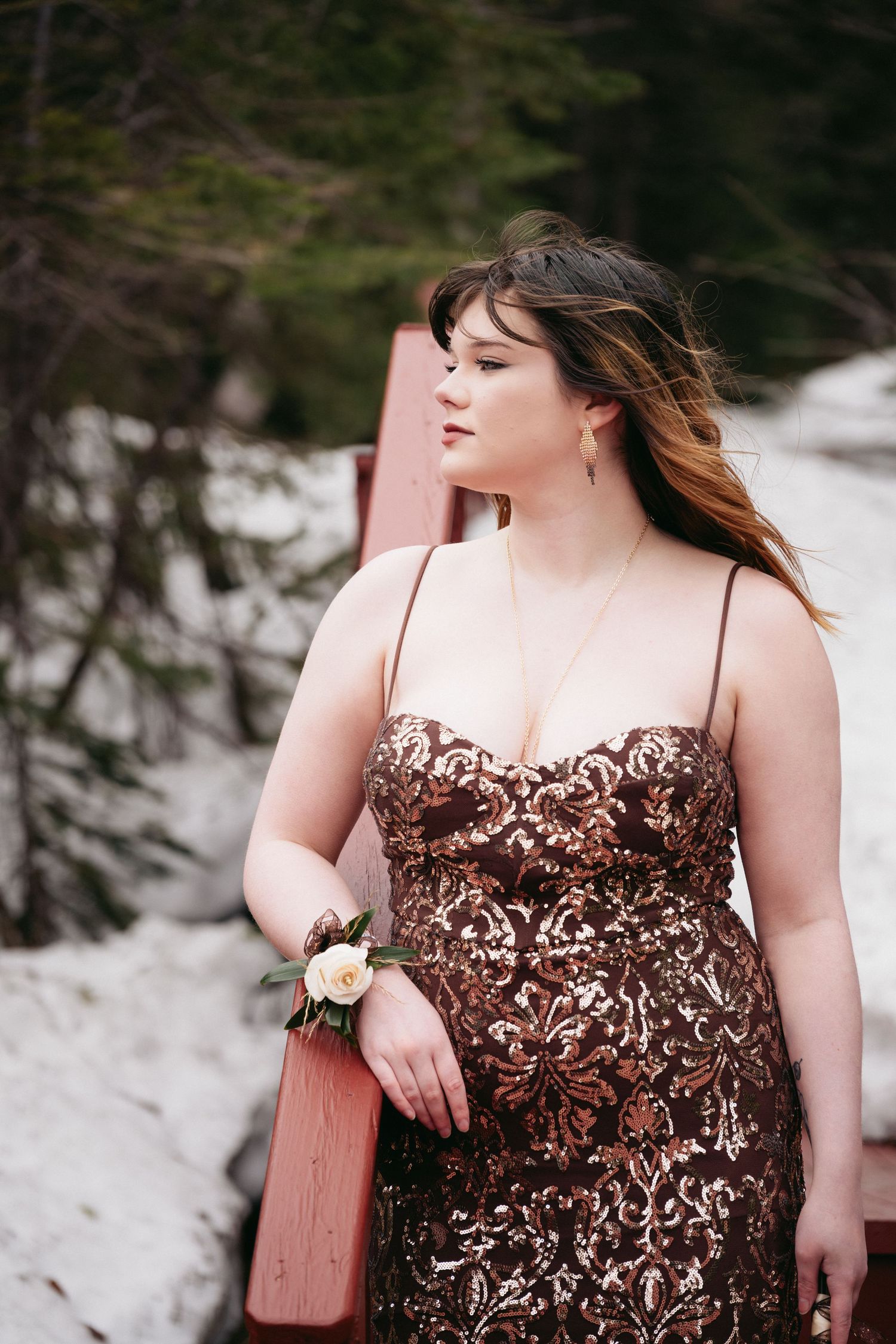 Young woman in brown sequin gown with floral wrist corsage poses outdoors in snowy winter setting.
