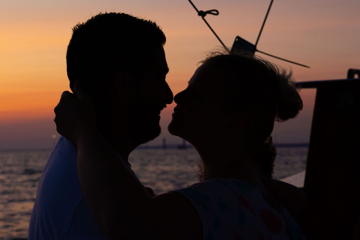 Romantic couple silhouetted against a vibrant orange sunset over the ocean, sharing an intimate moment.