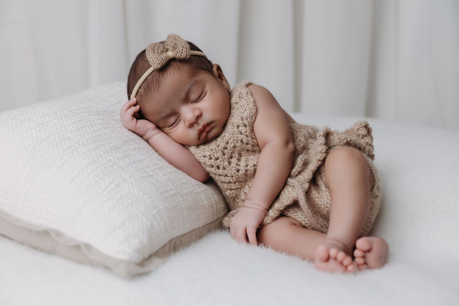 Peaceful newborn baby sleeping in knitted outfit on white pillow in studio portrait.