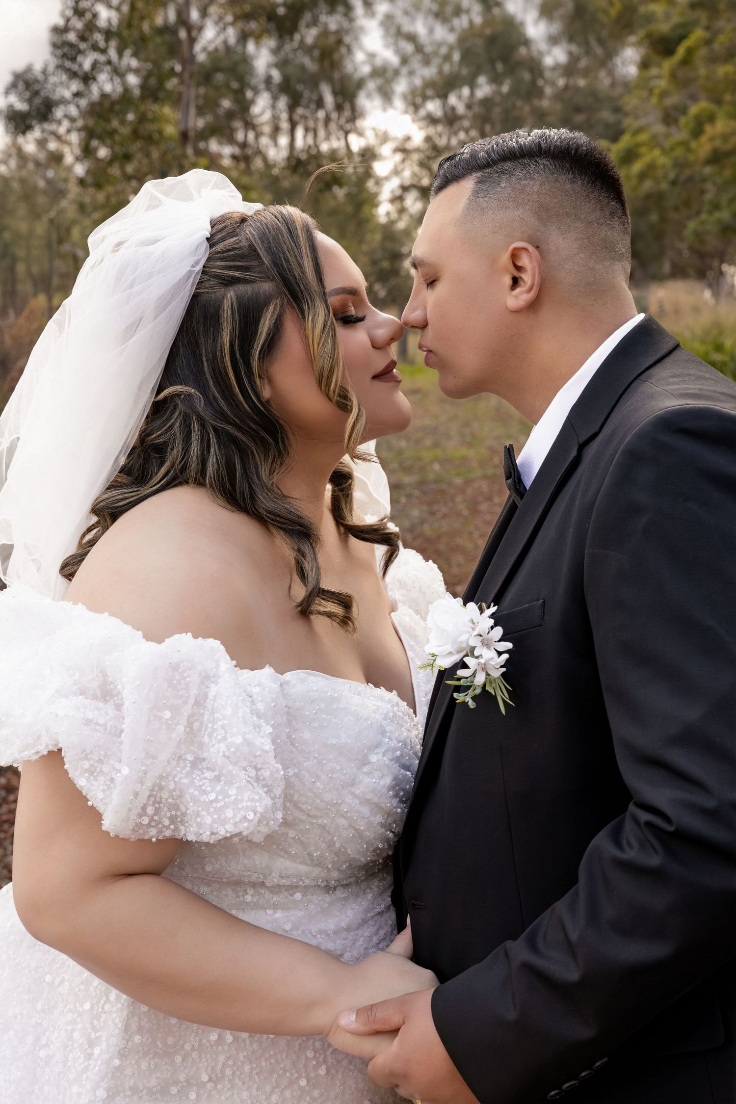 Bride and groom sharing romantic almost-kiss moment outdoors on their wedding day.