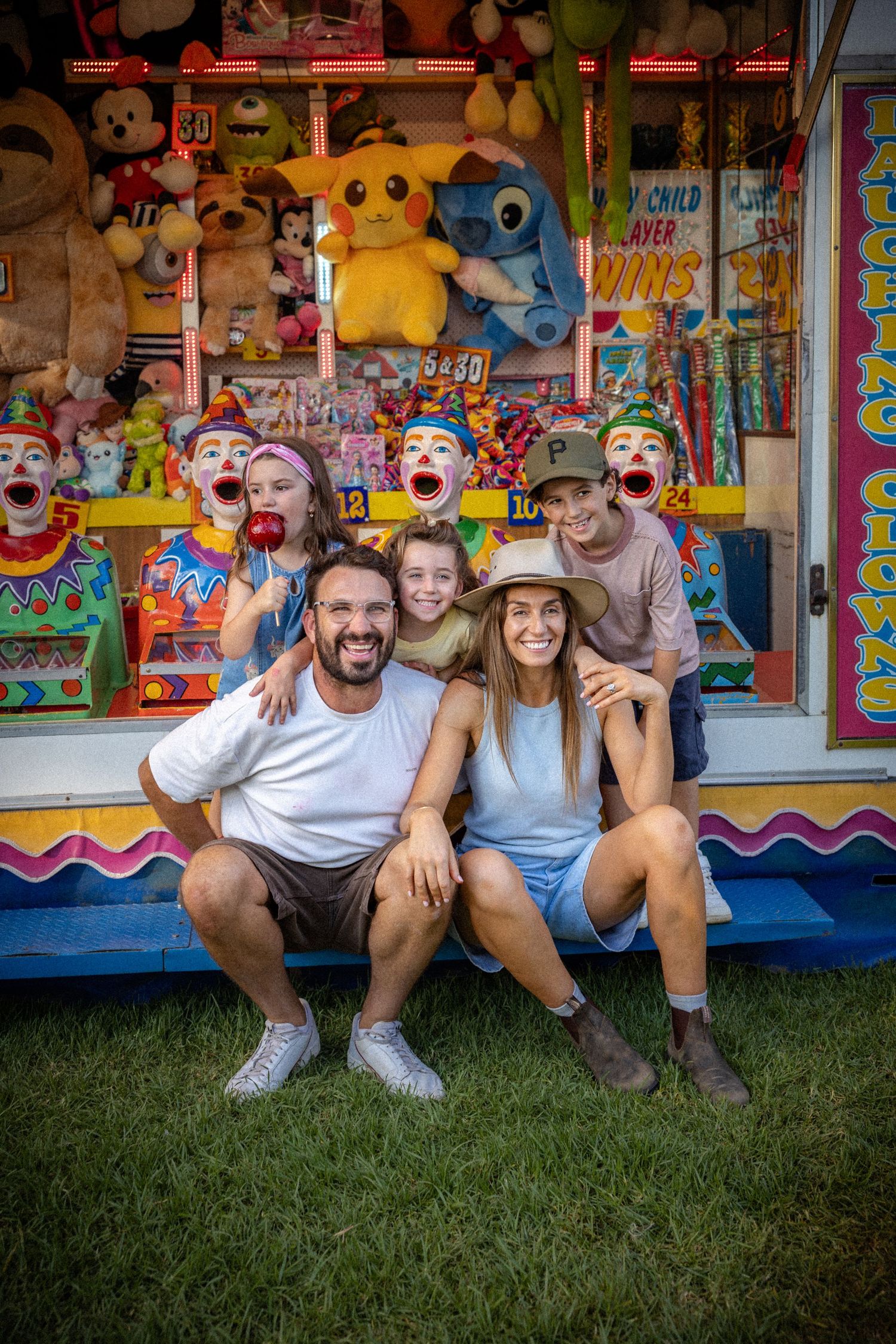 Happy family of five posing in front of colorful carnival clown game booth.